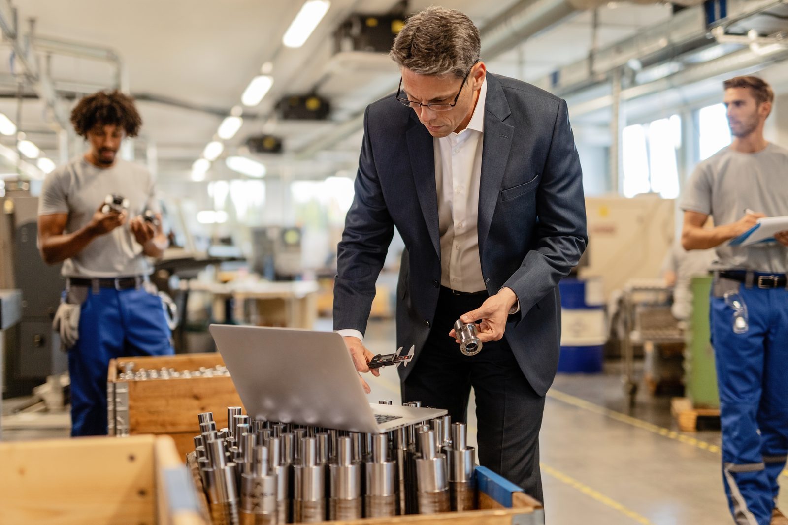 Responsable d'usine vérifiant les mesures d'un boulon d'acier devant un ordinateur